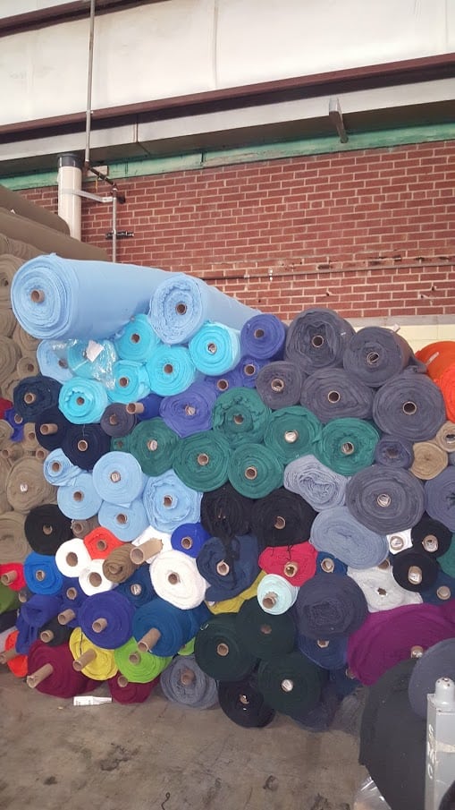 surplus fleece fabric in variety of colors stacked on top of each other with a brick wall in the background. 